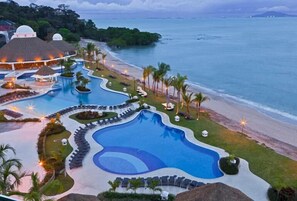 Un resort con una amplia piscina, zonas de descanso en la playa y vistas al océano.