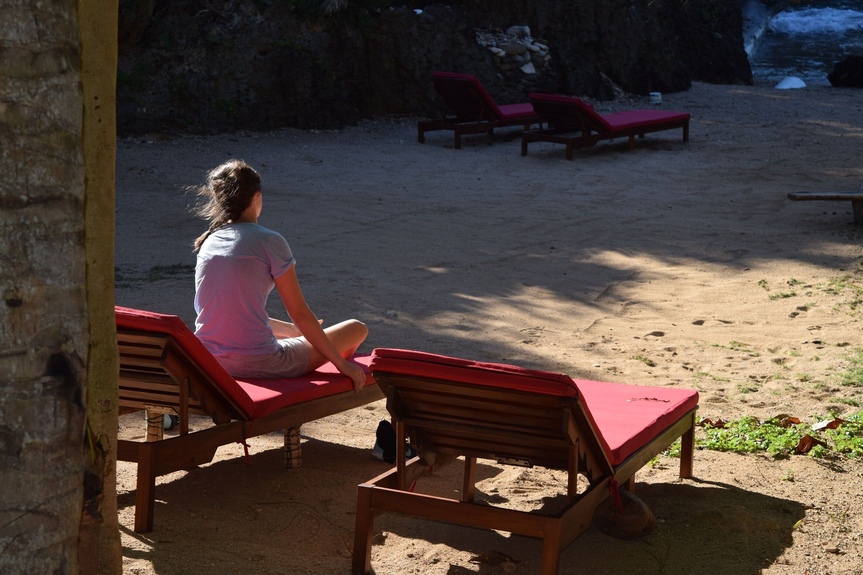 Une plage avec des chaises longues en bois, et une personne assise sur l’une d’elles.