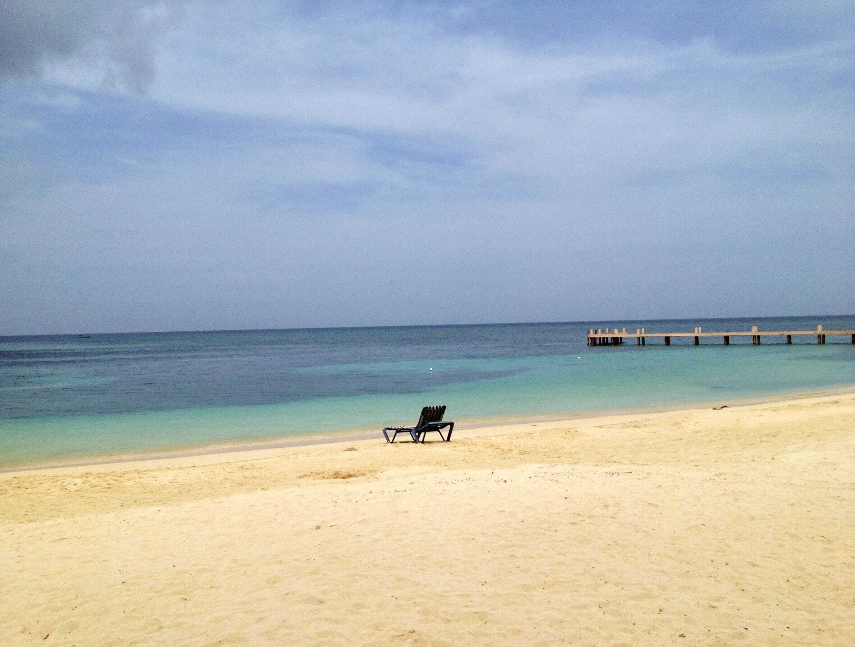 Una spiaggia con una sola sedia a sdraio nera e un molo di legno che si protende verso l'acqua.
