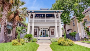 Uma casa de dois andares com varanda frontal, colunas e uma porta azul.