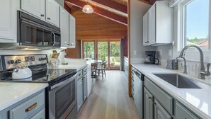 A modern kitchen with white cabinets, stainless steel appliances, and a wooden ceiling.