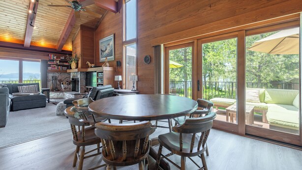 A spacious living area with a round wooden table and chairs, a fireplace, and a large window overlooking a lush garden.