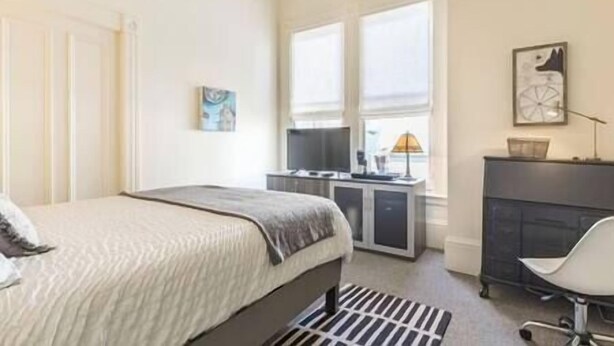 A bedroom with a bed, a desk with a computer, a chair, and a window. - Pacific Heights Victorian Bedroom & Bathroom (SF)