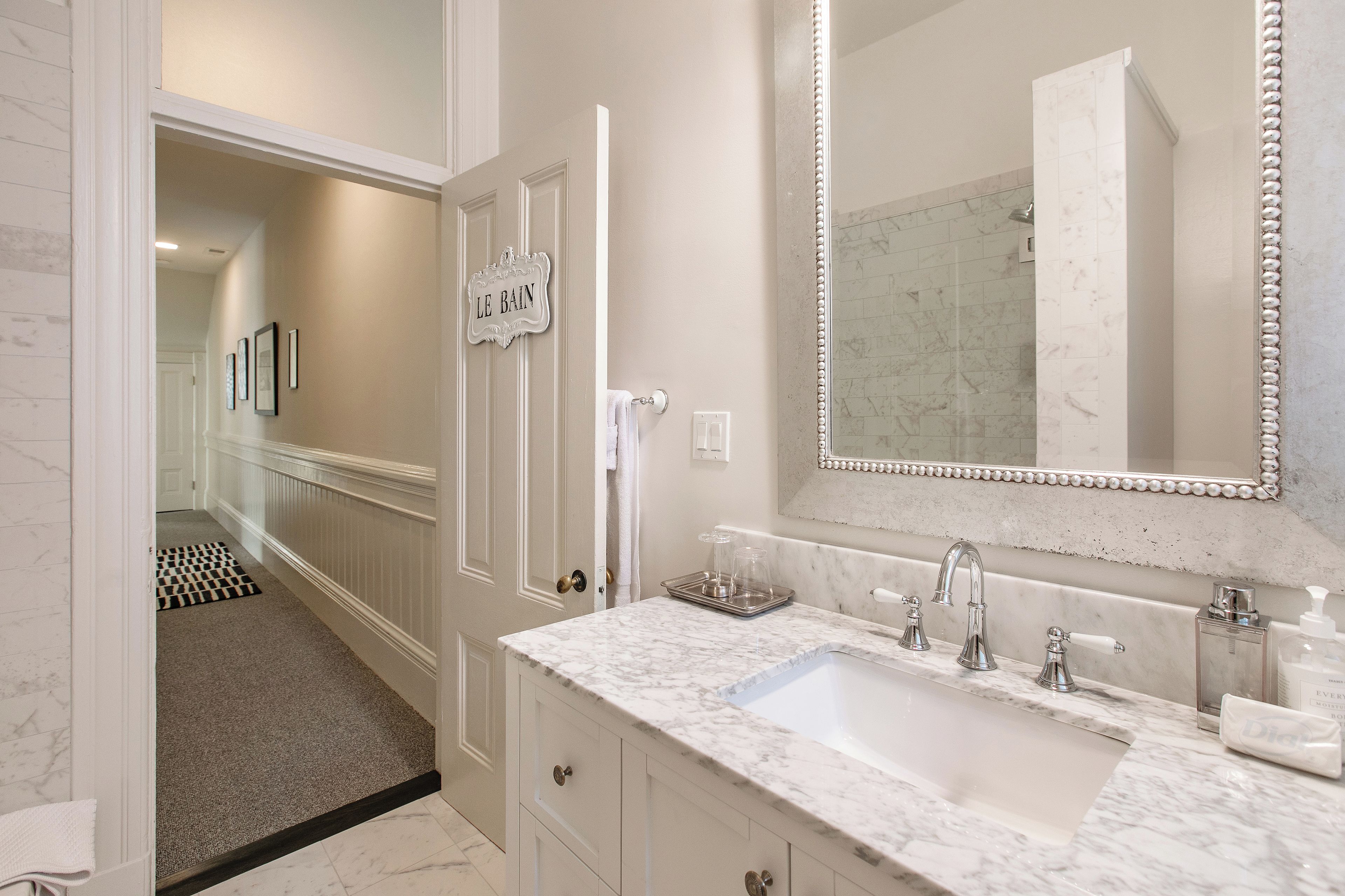 A bathroom with a marble sink, a large mirror, and a sign that reads 'LE BAIN'.