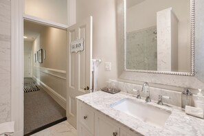 Un bagno con un lavabo in marmo, un ampio specchio e un segnale con la scritta 'LE BAIN'.