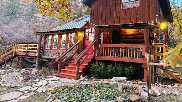 Une cabane en bois rustique, dotée d’une véranda, d’un escalier et d’un petit jardin.