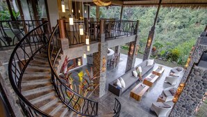 Un intérieur à plusieurs niveaux, agrémenté d’un escalier en colimaçon, de piliers en pierre et d’espaces extérieurs aménagés pour se détendre, offrant une vue sur une végétation luxuriante.