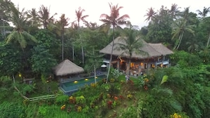 Un complexe hôtelier doté de bâtiments à toits de chaume, d’une piscine et d’une végétation tropicale luxuriante.