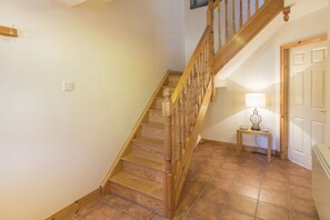 A wooden staircase with a handrail leading to a landing. A table lamp is on the landing table, and a door is visible in the background. - Spacious Comfortable Holiday Home in the Heart of Dingle (Dingle)