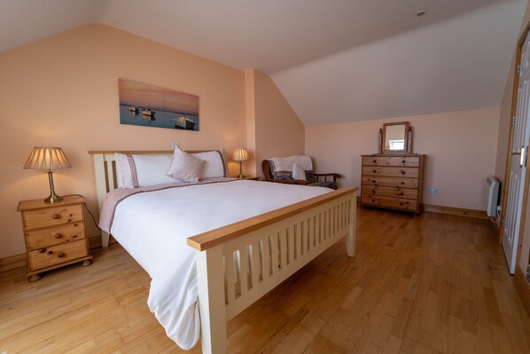A bedroom with a wooden bed, a nightstand with a lamp, a dresser, and a painting on the wall. - Spacious Comfortable Holiday Home in the Heart of Dingle (Dingle)