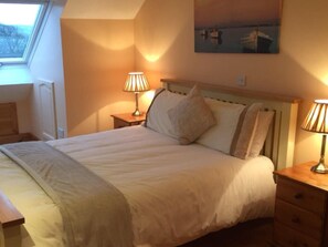 A bedroom with a bed, two bedside tables with lamps, a painting on the wall, and a window with a view of trees. - Spacious Comfortable Holiday Home in the Heart of Dingle (Dingle)