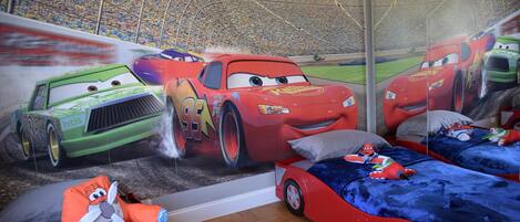A children's bedroom with a race car theme, including a mural, themed bedding, and a toy car.