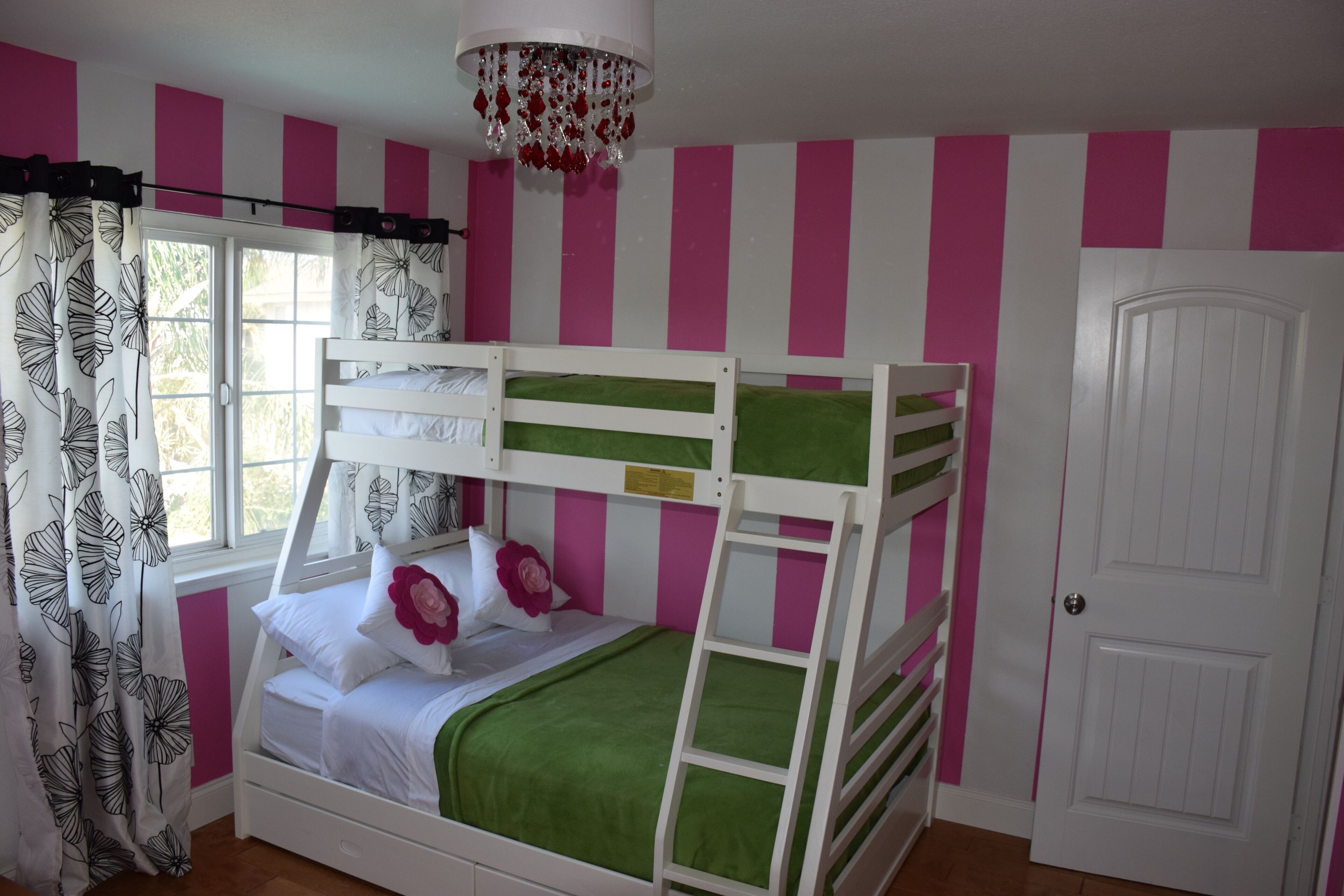 A bunk bed room with pink and white striped walls, a white door, and a window with curtains.