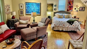 A cozy room with a bed, two armchairs, a red sofa, and a wooden coffee table.