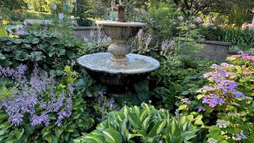 Un jardín con una fuente de piedra central rodeada de exuberante follaje y diversas plantas con flores.