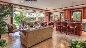 Amplia sala de estar con sofá, sillas, comedor con taburetes de bar y cocina con alacenas de madera y microondas.