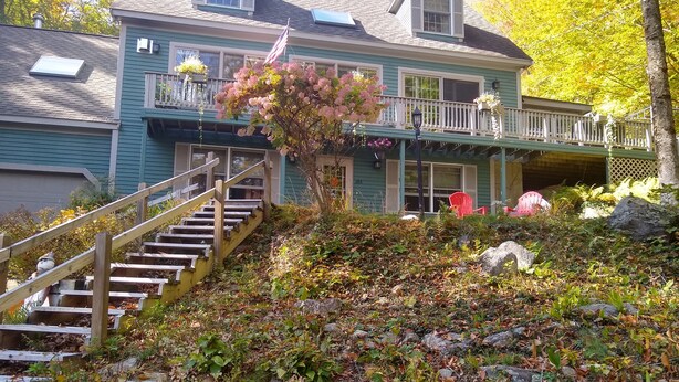 A two-story house with a wooden staircase leading to a porch. - Quiet, clean, and comfy: Centrally Located In The Mt. Washington Valley. (Intervale)