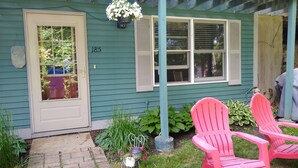 A house with a front door, two windows with shutters, a porch with a hanging flower pot, and two pink chairs. - Quiet, clean, and comfy: Centrally Located In The Mt. Washington Valley. (Intervale)