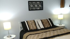 A neatly made bed with patterned bedding, two bedside tables with lamps, a wall art piece, and a window with a curtain. - Quiet, clean, and comfy: Centrally Located In The Mt. Washington Valley. (Intervale)