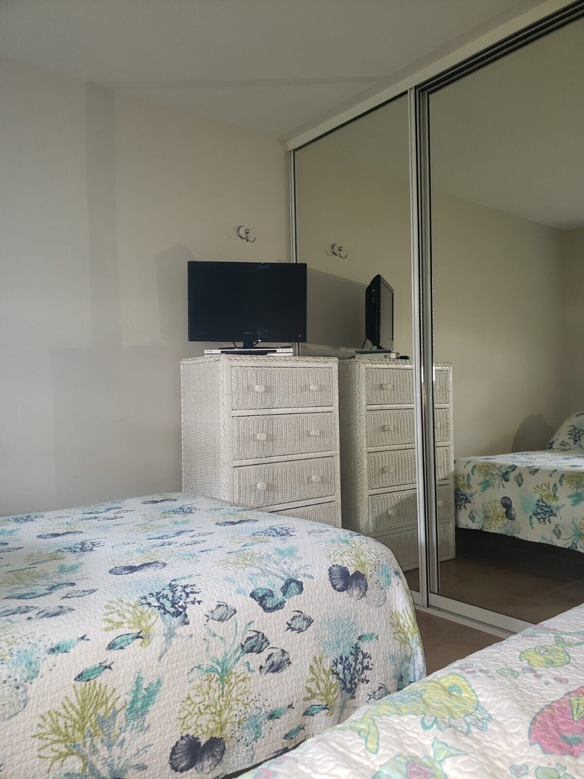 Un dormitorio con dos camas, un televisor sobre una cómoda y un espejo grande.