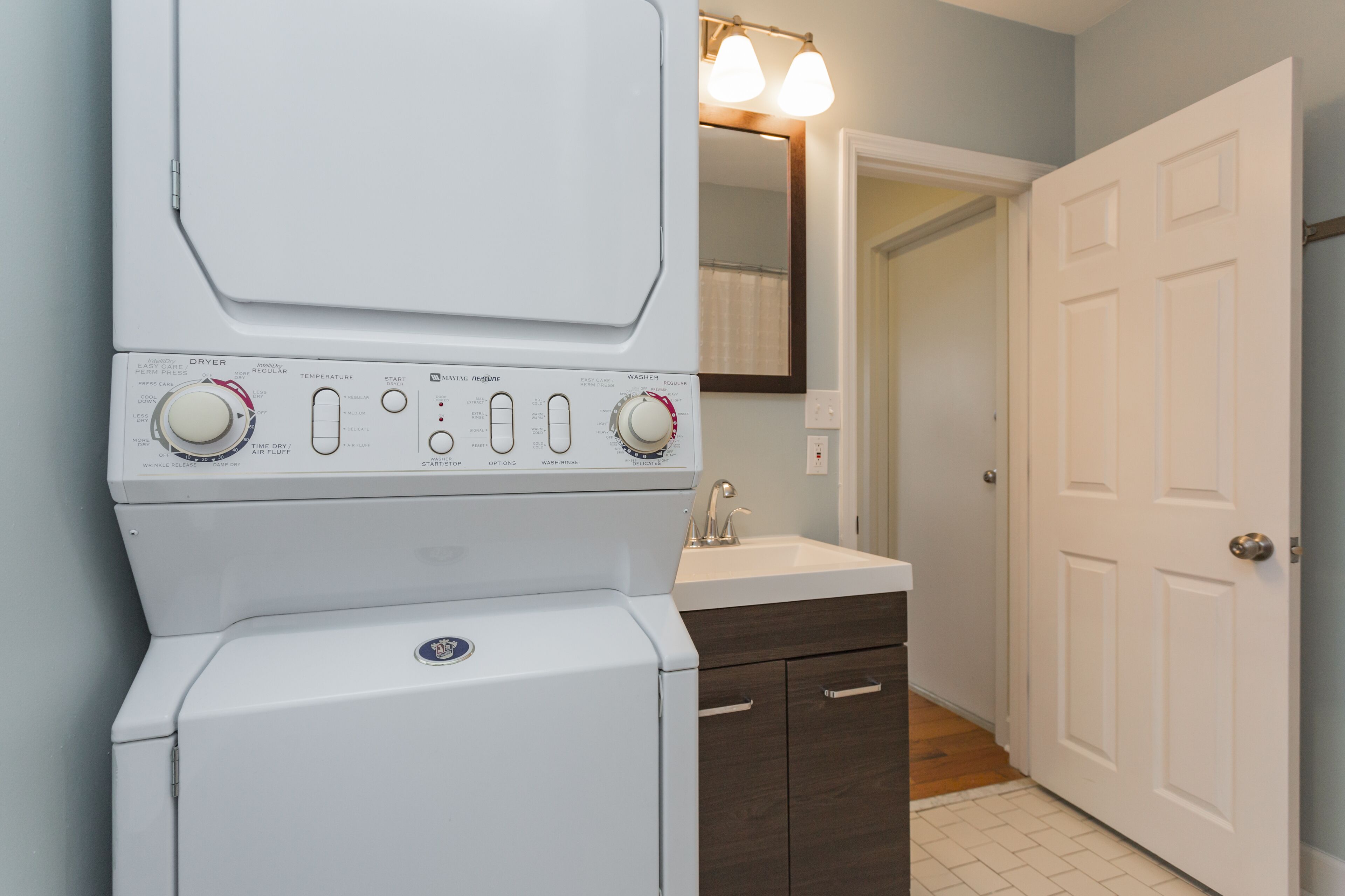 A compact washer and dryer unit with a control panel featuring temperature and time settings, located in a bathroom with a sink and a mirror.