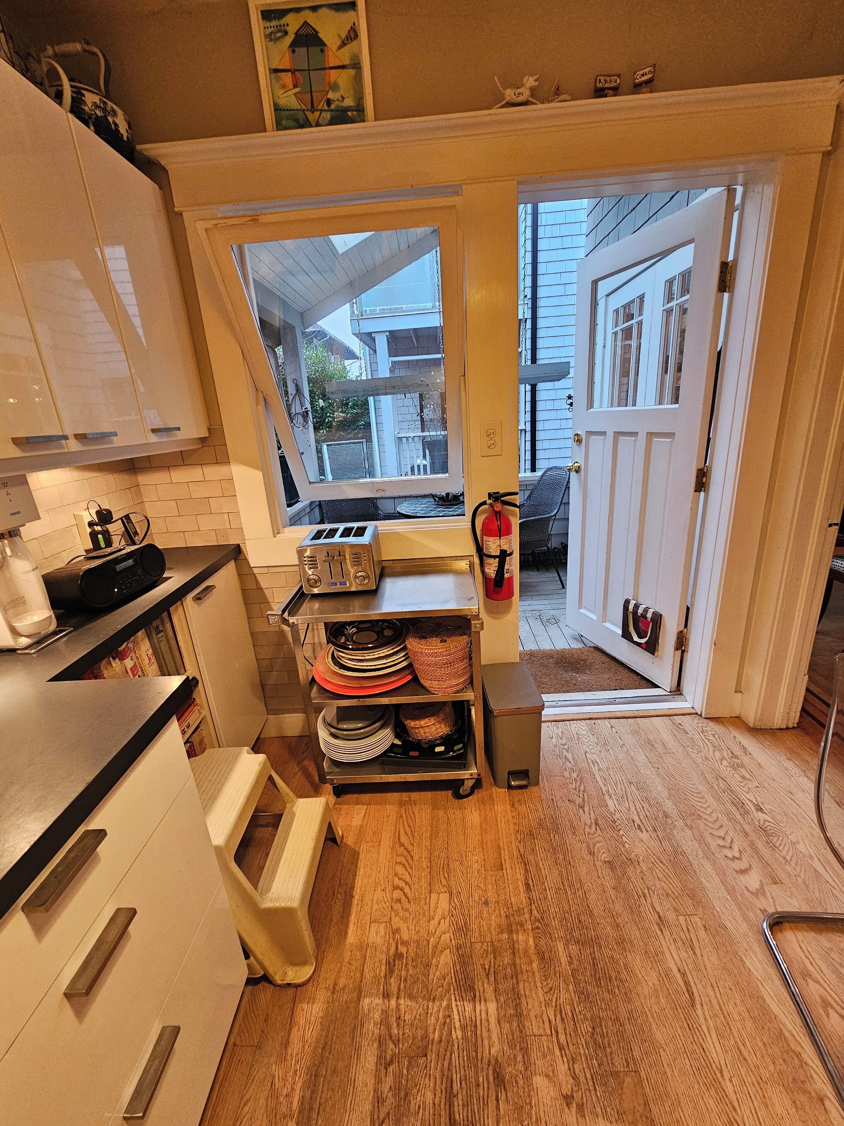 A compact kitchen with a window, a toaster, a fire extinguisher, and a small trash bin.
