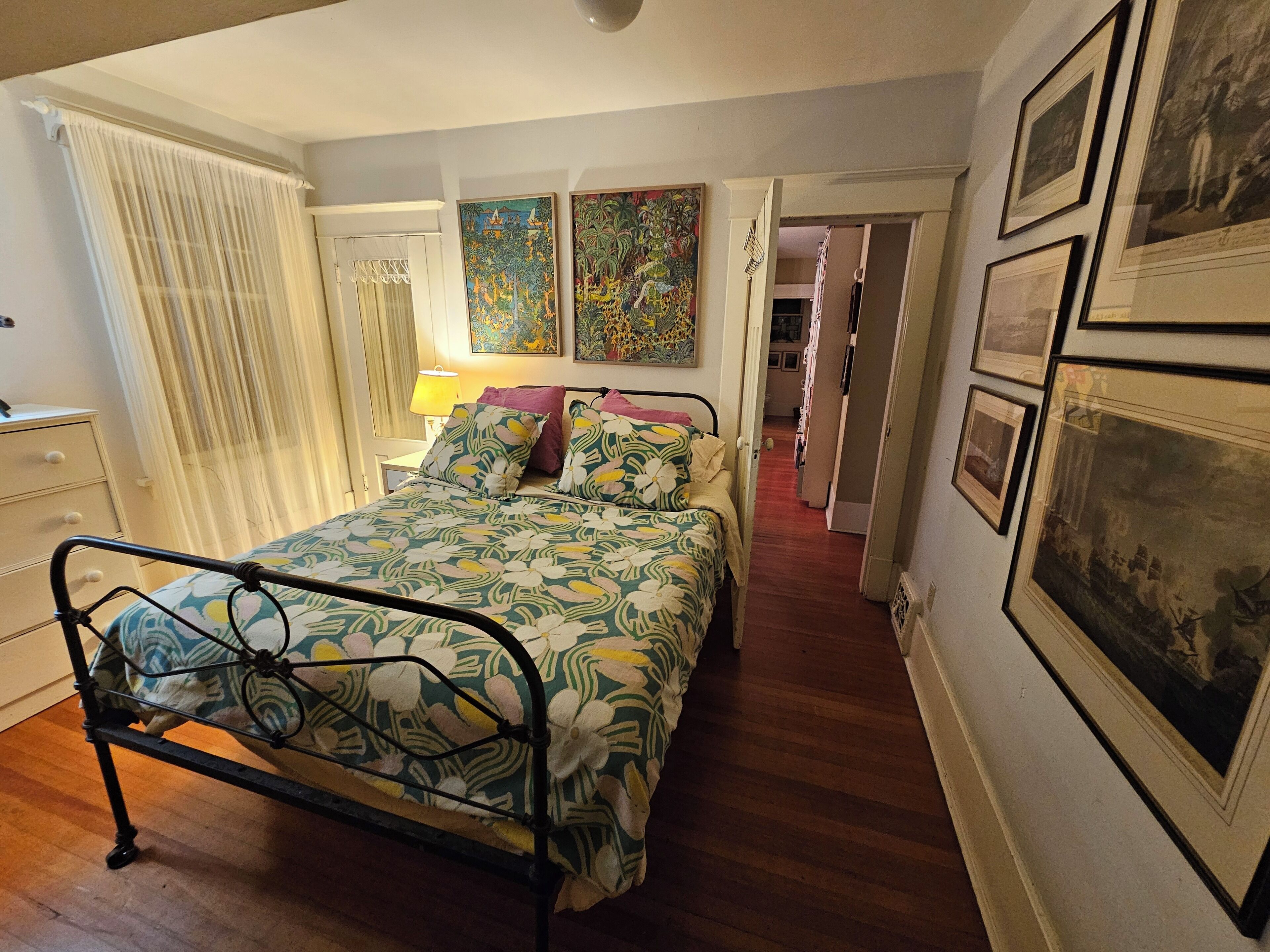 Un dormitorio con cama, mesita de noche, lámpara y puerta que da a otra habitación.