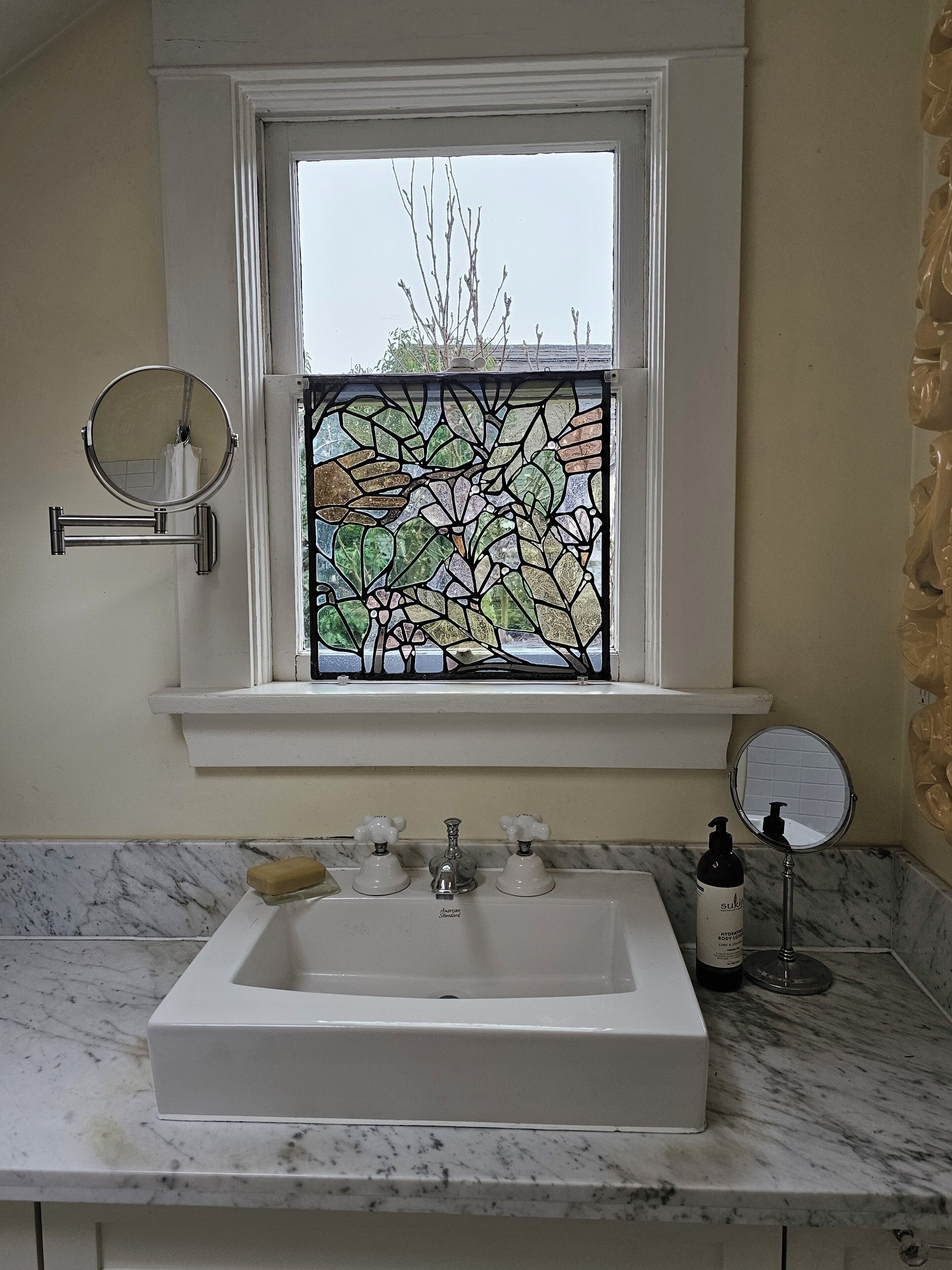 A bathroom with a large window, a sink, and two mirrors.