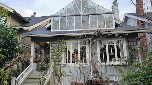 Ein Haus mit einem großen Glashaus, einer Veranda mit Stufen und einem Garten mit verschiedenen Pflanzen.