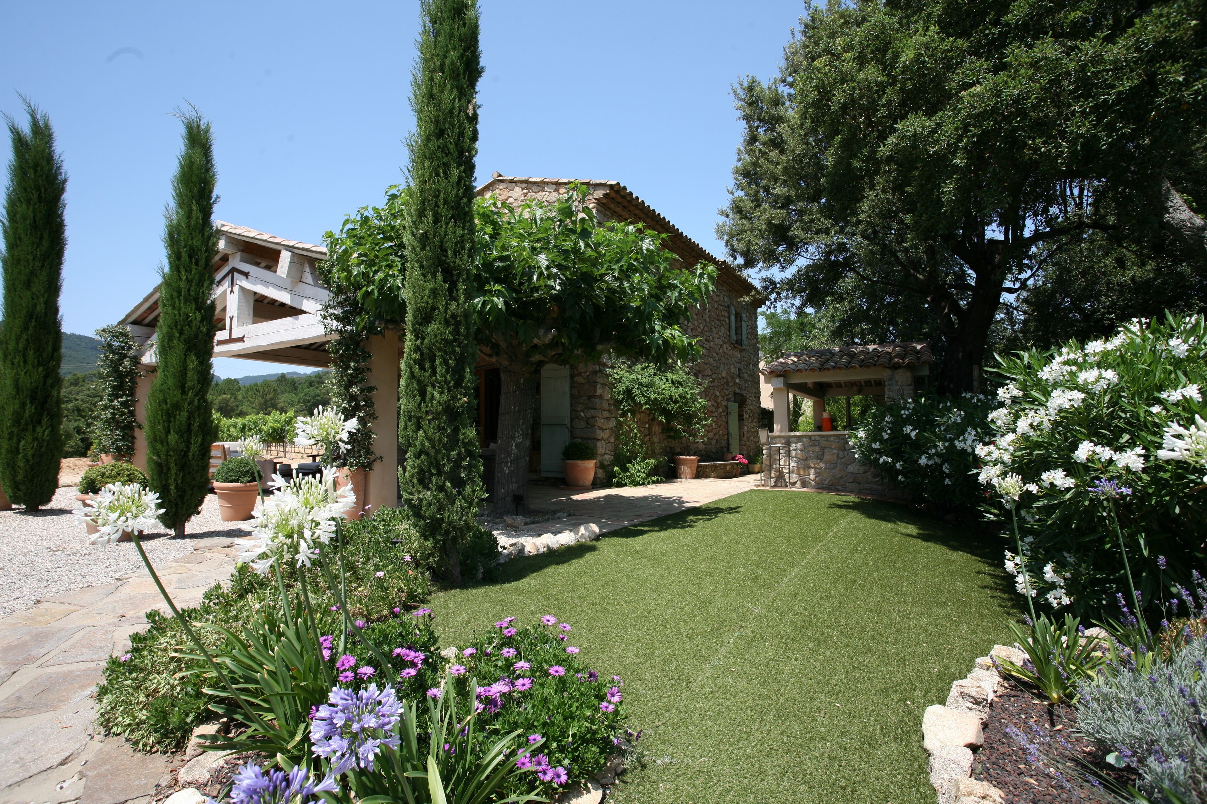 A stone house with a garden featuring a lawn, potted plants, and flowers.