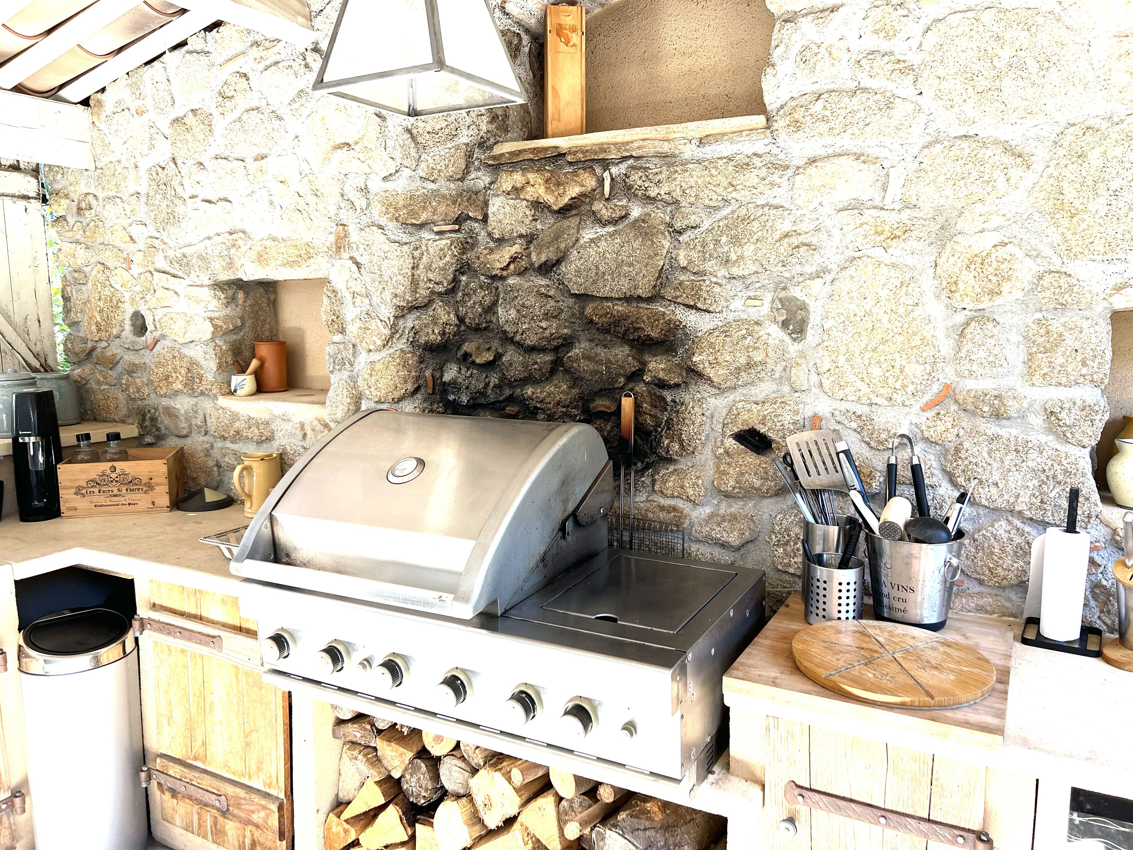 A stone wall with a grill and cooking utensils.
