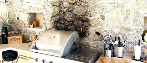 A stone wall with a grill and cooking utensils.