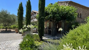 A stone building with a tiled roof, surrounded by lush greenery and flowering plants.