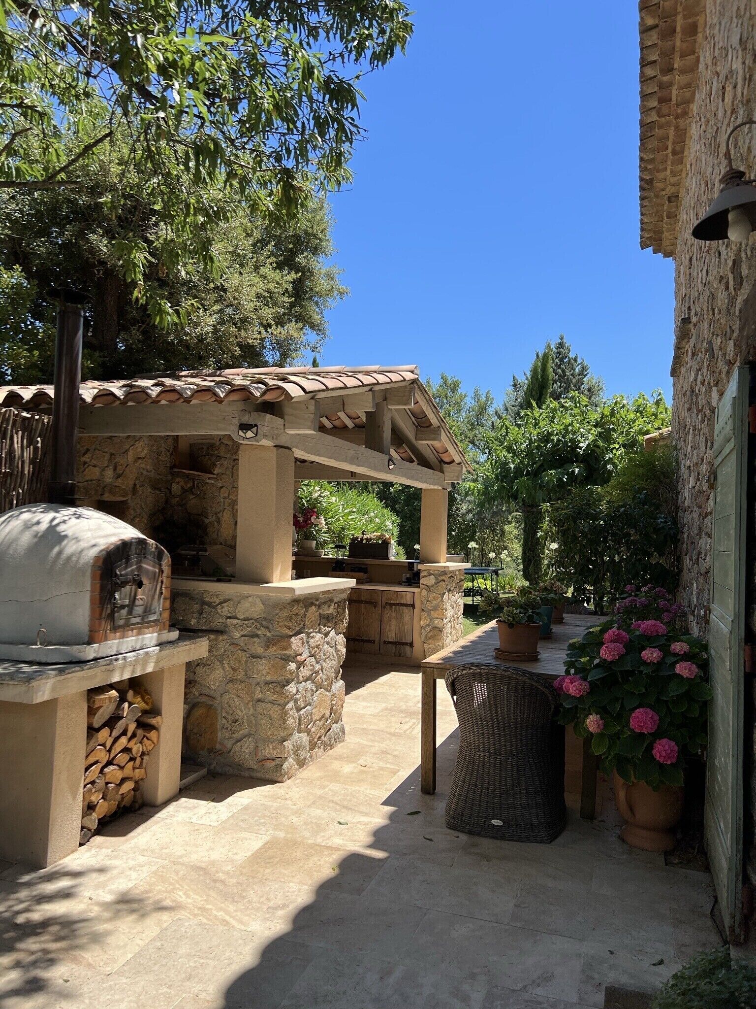 An outdoor patio with a stone oven, a wooden pergola, and potted plants.