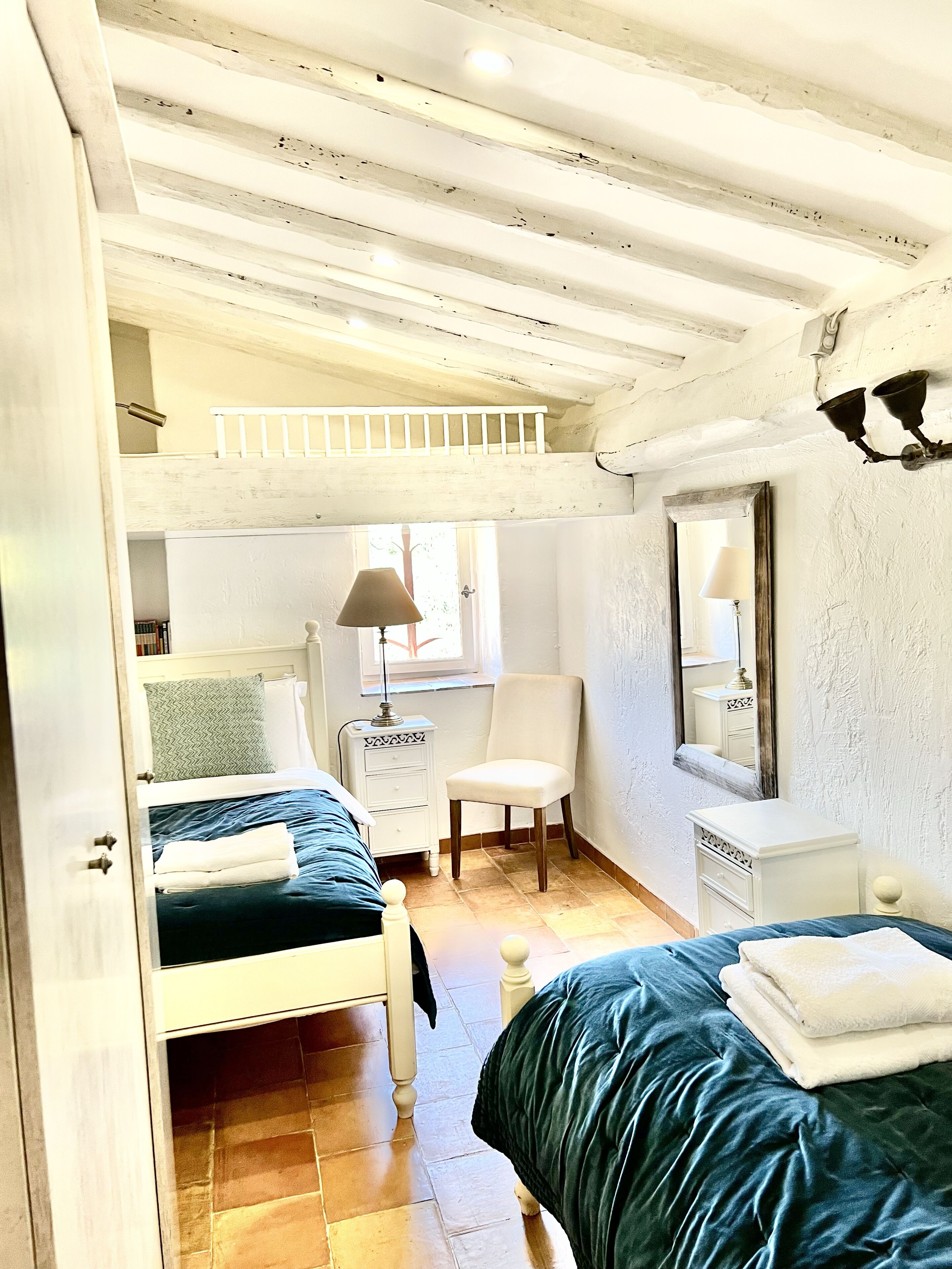 Una habitación con una cama individual superior e inferior, una silla, una mesita de noche, un espejo y una ventana.