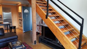 A modern living room with a wooden staircase, a black entertainment unit, and a blue door. - Cool Downtown Orenco Loft (Hillsboro)