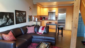 A modern living room with a leather sofa, a coffee table, and a kitchen area with wooden cabinets and stainless steel appliances. - Cool Downtown Orenco Loft (Hillsboro)