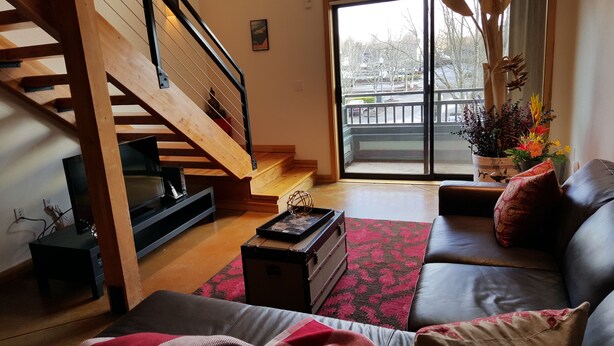 A living room with a wooden staircase, a sofa, a coffee table, and a television. - Cool Downtown Orenco Loft (Hillsboro)