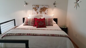 A neatly made bed with a white comforter and plaid bedding, a world map on the wall, and a small table with a green vase. - Cool Downtown Orenco Loft (Hillsboro)