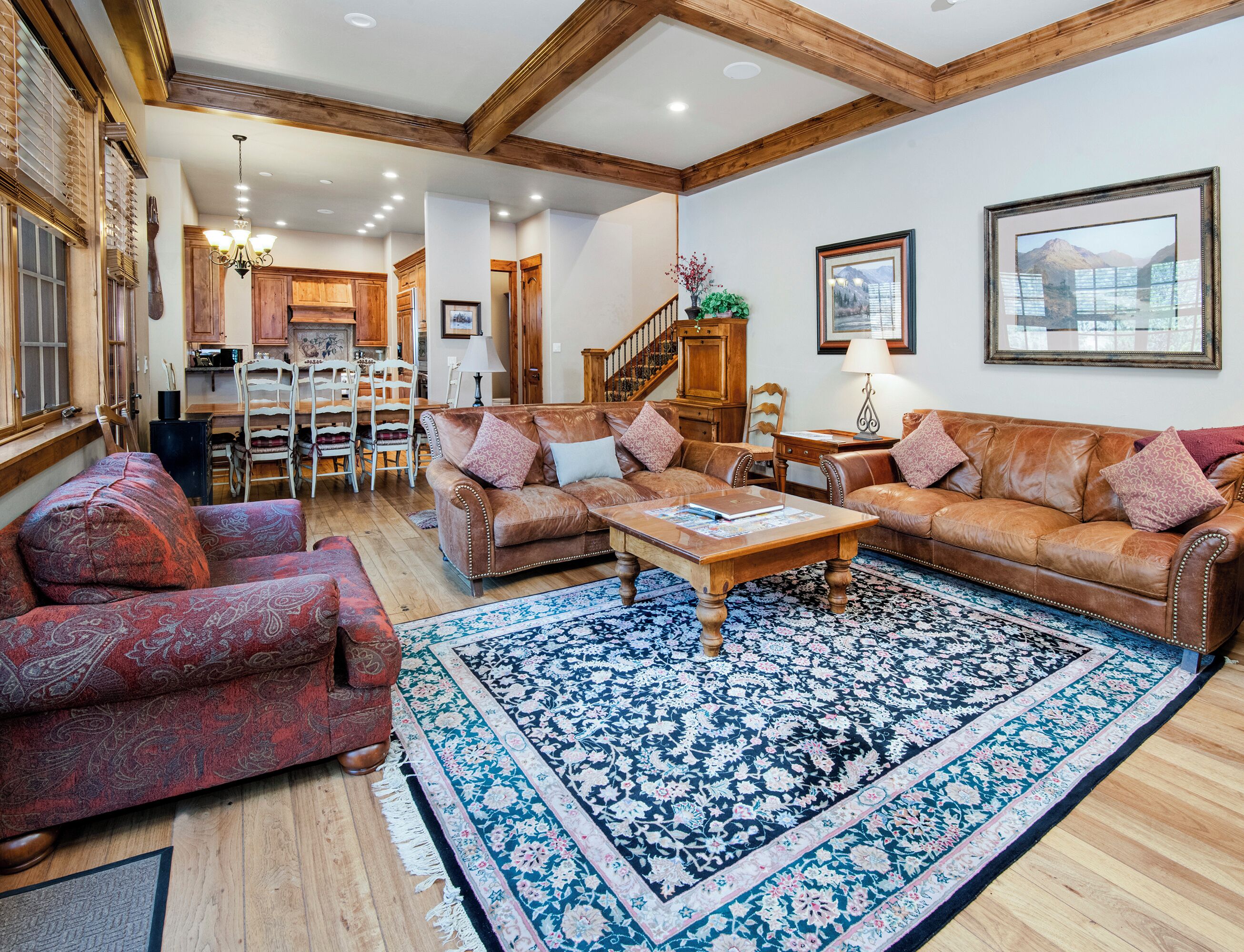 A spacious living room with a large brown leather sofa, a matching armchair, and a coffee table. A wooden staircase leads to an upper level.