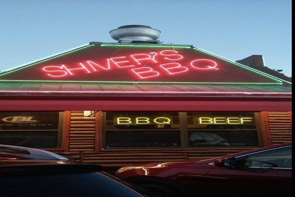 En restaurang med en neonreklamskylt där det står ”Shiner’s BBQ” och ”BBQ Beef” på fönstren.
