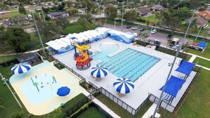 Luftaufnahme eines Schwimmbadkomplexes mit großem Pool, einer Wasserrutsche und zahlreichen Strandsonnenschirmen.