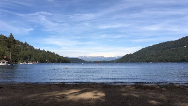 Un lac avec des bateaux, un kiosque et une colline boisée.