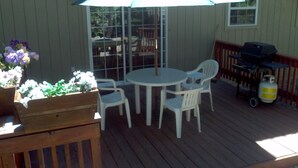 Une terrasse avec une table ronde et des chaises, un barbecue et un jardinier en bois orné de fleurs.
