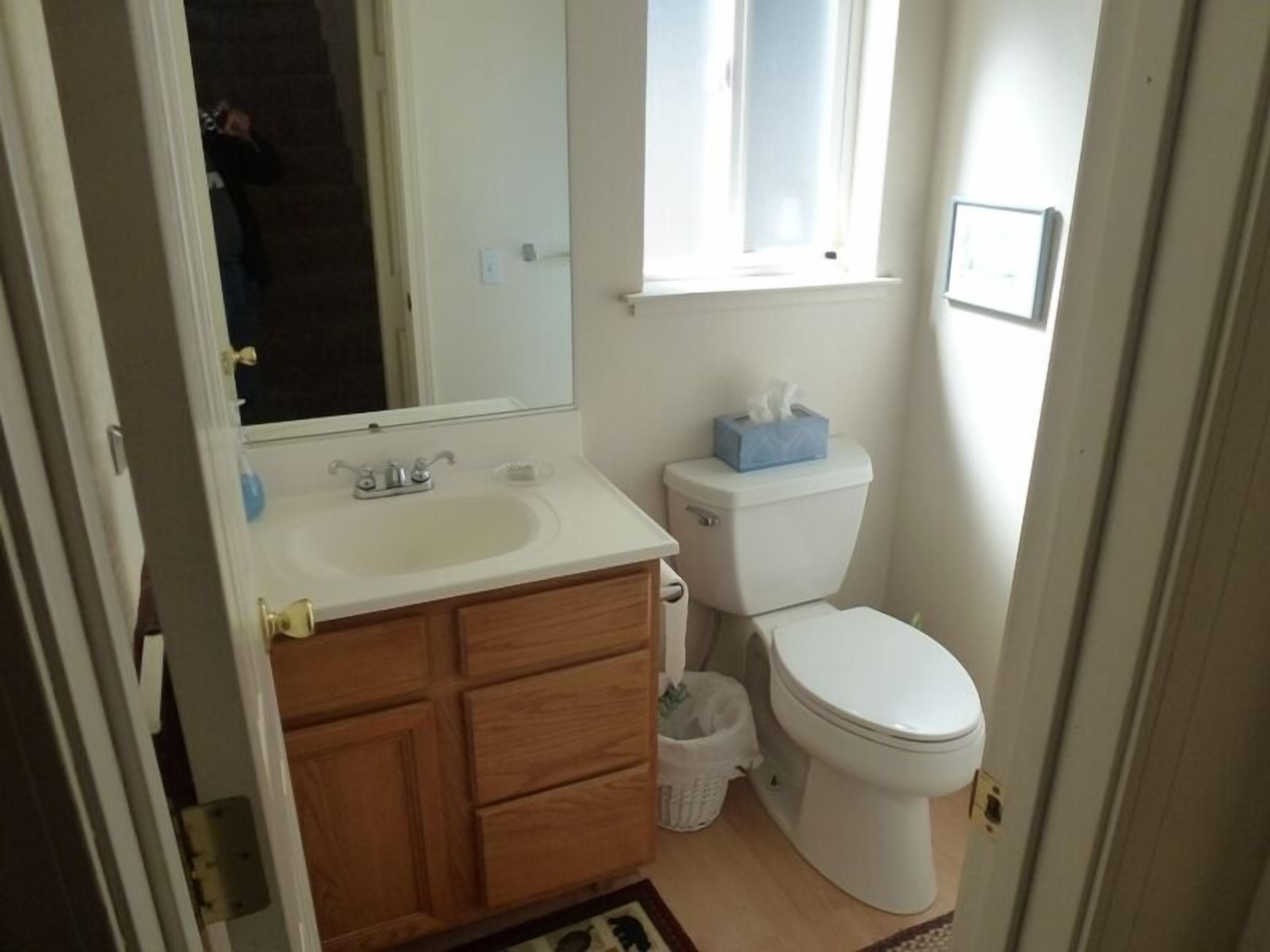 Une petite salle de bain avec un lavabo blanc, un meuble-lavabo en bois, des toilettes et une fenêtre.