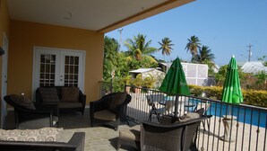 A covered outdoor area with wicker furniture, a pool, and green umbrellas.