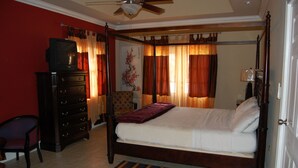 A four-poster bed with a wooden frame, a dresser with drawers, a chair, and a ceiling fan.