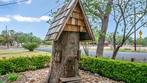 Una casa en un árbol con techo de madera y una puerta pequeña, rodeada de follaje y un camino de grava.