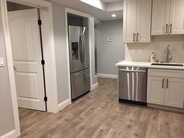 A modern kitchen with stainless steel appliances, white cabinetry, and a wooden floor.