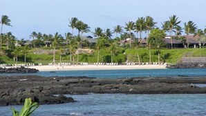 Ein Strand mit felsigem Ufer, Palmen und einem Resort im Hintergrund.